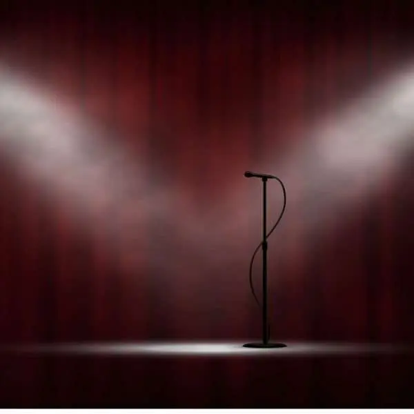 Microphone standing on stage in spotlight, red curtain background.